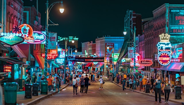 A vibrant street scene on Beale Street in Memphis at night, with colorful neon signs and crowds of people walking along the street.