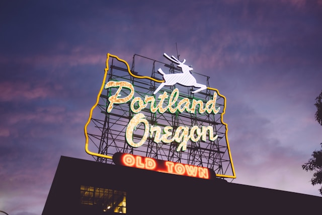 A neon sign reading 'Portland Oregon' with a white stag on top, set against a twilight sky, above the words 'Old Town' in red.